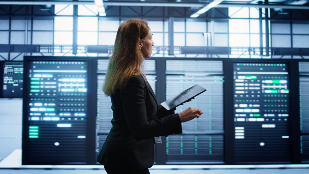 Engineer in server hub checking recovery plan on tablet, monitoring rackmounts energy consumption. Woman in data center making sure rigs are functioning optimally, doing routine disk checks, camera B